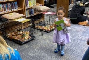 Toddler in lavender dress holding book crates stations in background